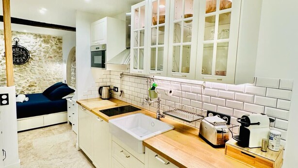 A modern kitchen with white cabinets, a stone wall, a wooden ceiling, and a built-in oven. - 1539891003 TOWNHOUSE STUDIO 2 (Cannes)