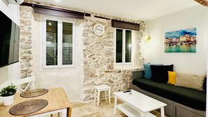 Tunnelmallinen olohuone, jossa on kiviseinä, puukatto, sohva, sohvapöytä ja ruokapöytä, jonka päällä on alustat.