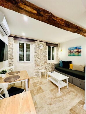 Ein gemütlicher Wohnbereich mit Steinwand, Holzboden, einer Couch, einem Couchtisch und einem Esstisch mit Platzdeckchen.
