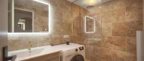 Un baño moderno con lavadora integrada, un espejo grande y cabina de ducha.