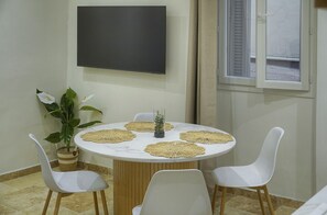 Une table ronde entourée de quatre chaises blanches, un pot de fleurs et des sets de table en fibres tressées.