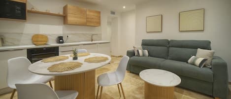 A modern kitchen with a dining area, a sofa, and two framed artworks on the wall.