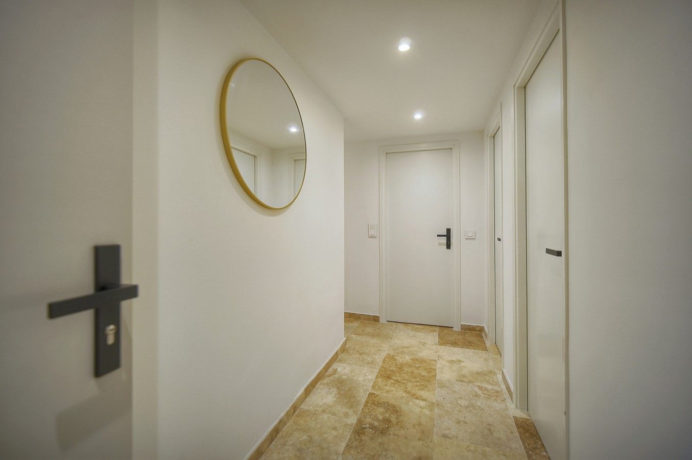 Un pasillo con un espejo redondo en la pared, una puerta con manija y piso de baldosas.