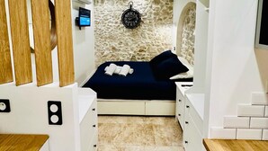 Una habitación pequeña con cama, pared de piedra, un reloj y televisión.