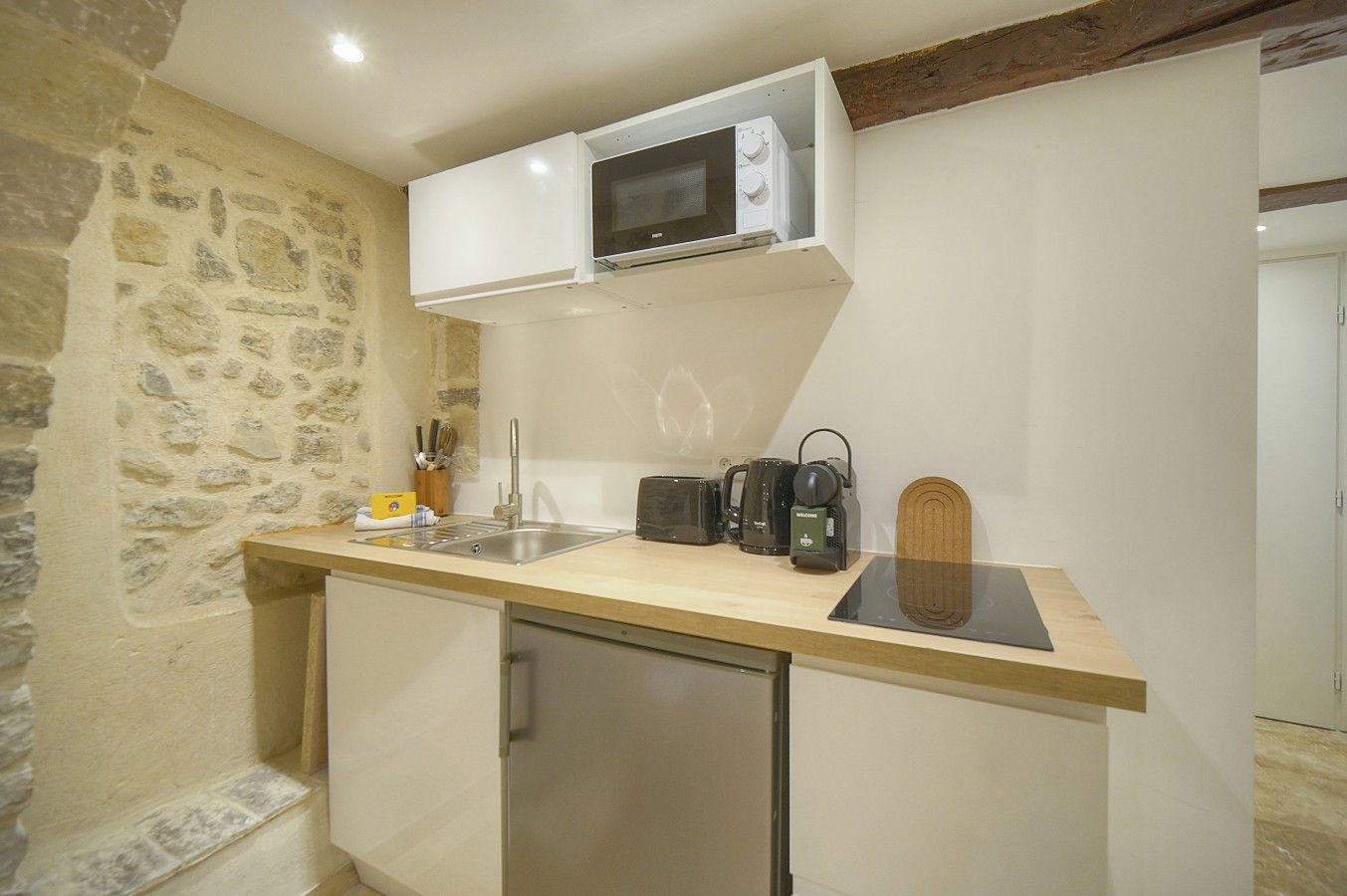 A compact kitchen with a microwave, toaster, kettle, and coffee maker on the counter.