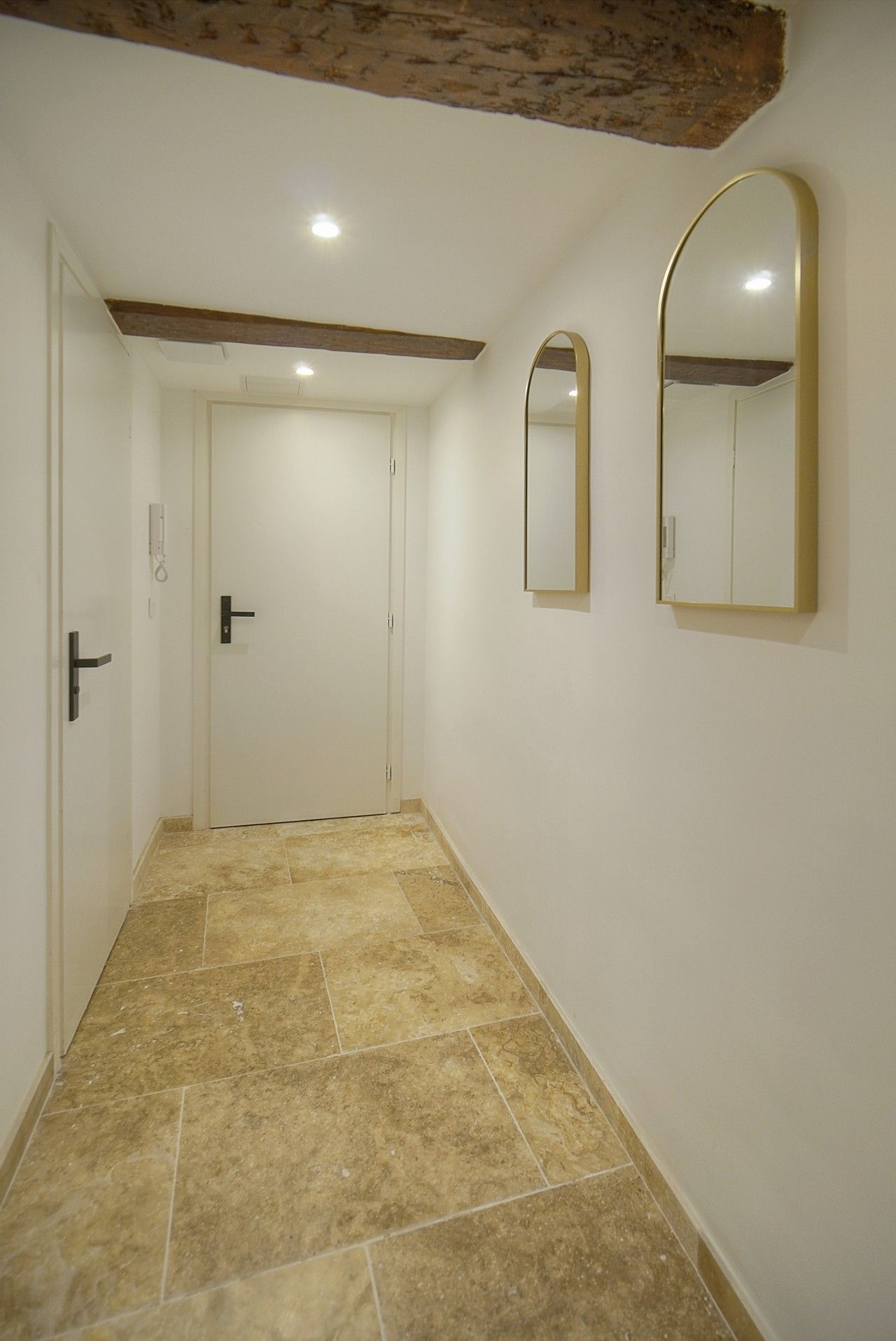 A hallway with a tiled floor, a door with a black handle, and two wall-mounted mirrors.