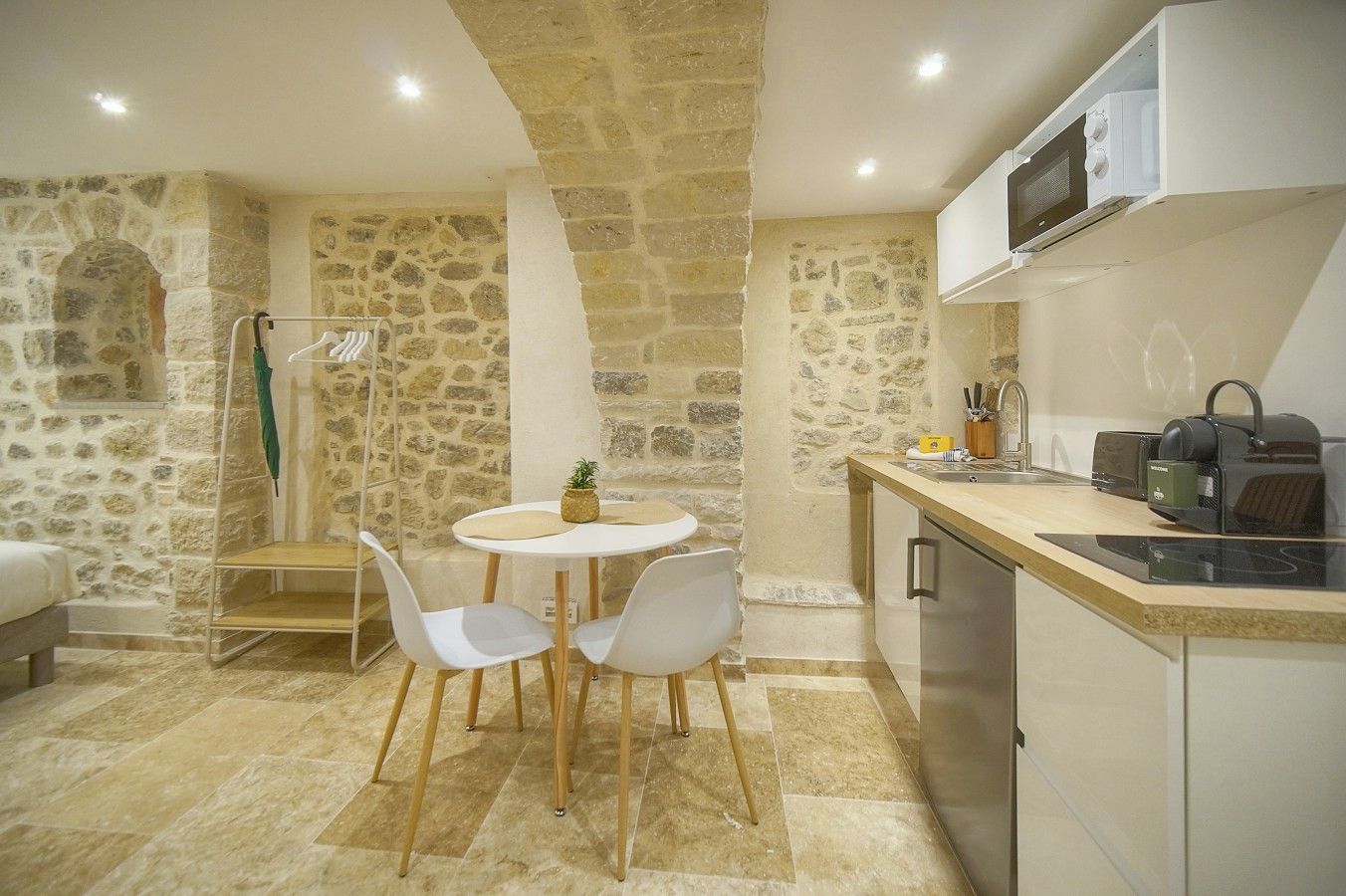 A modern kitchen with stone walls, a round table, white chairs, and a built-in microwave.