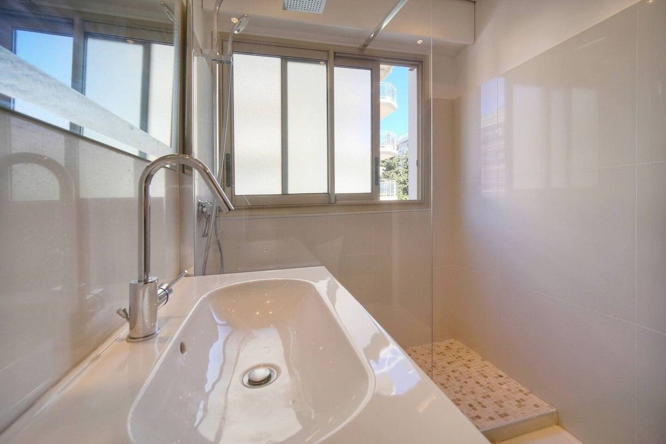 A modern bathroom with a large sink, a shower, and a window providing natural light.