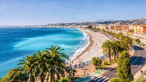 A coastal cityscape with a beach, palm trees, and a road with pedestrians. - 15014938 FRGK GOUNOD Studio Modern AC Wi-Fi Fiber (Nice)
