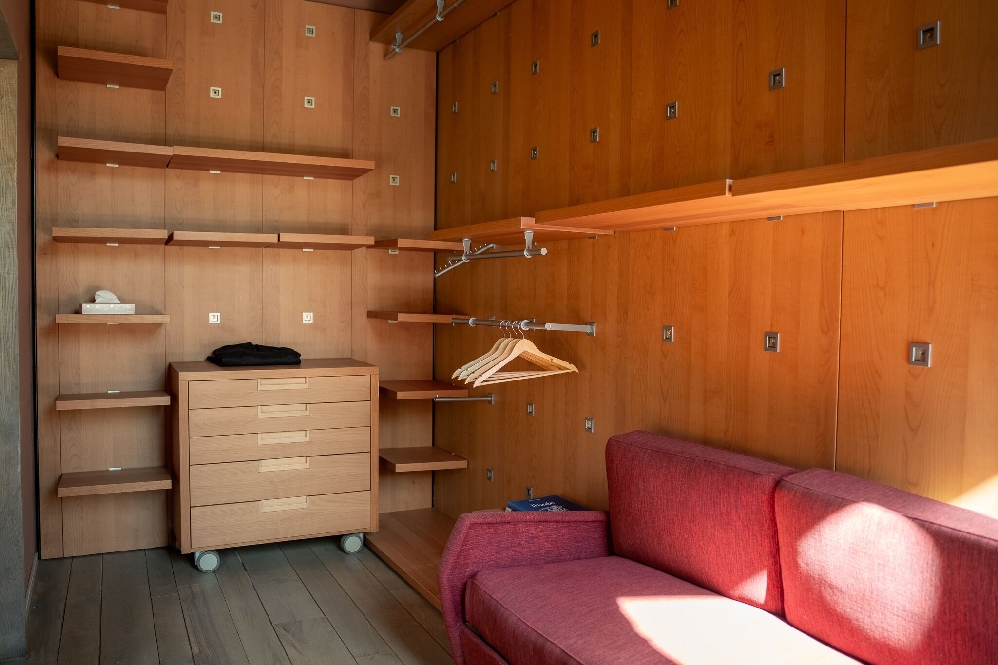 Une pièce avec une armoire en bois, un canapé rouge et un petit bureau avec des tiroirs.