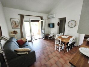A living room with a sofa, a dining table with chairs, a TV, and a clock on the wall. - Fully Equipped 2-Bedroom Apartment in the Gulf of St. Tropez (Cogolin)
