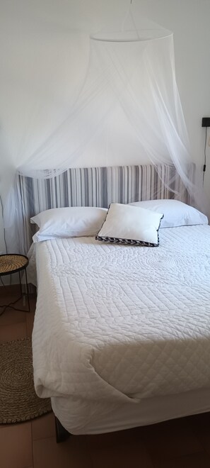 A bed with a white quilt, a canopy, striped curtains, and a small round table. - Fully Equipped 2-Bedroom Apartment in the Gulf of St. Tropez (Cogolin)