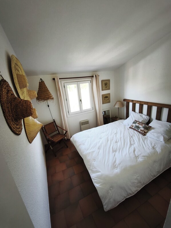 A bedroom with a bed, a chair, a window, and wall decorations. - Fully Equipped 2-Bedroom Apartment in the Gulf of St. Tropez (Cogolin)