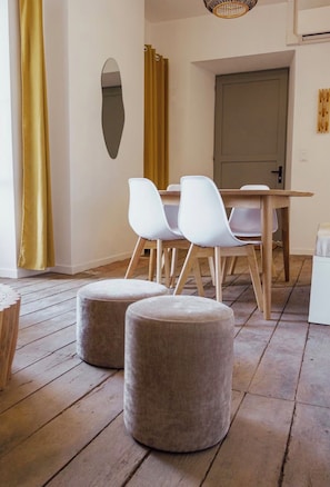 A dining area with a wooden table, white chairs, and two ottomans on a wooden floor. - 80 m² Vacation Rental + 20 m² Studio - Sleeps 8 - Puy du Fou (Mauléon)