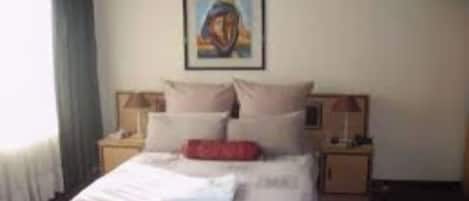 Una habitación de hotel con una cama, dos mesitas de noche, un cuadro en la pared y una ventana con cortinas.