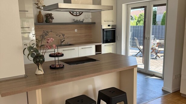A modern kitchen with a wooden countertop, two black stools, a built-in oven, and a sliding glass door leading to an outdoor area. - Carolingian Stay (Emmerich am Rhein)