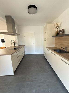 A modern kitchen with white cabinetry, a wooden countertop, a built-in oven, and a stainless steel sink. - Carolingian Stay (Emmerich am Rhein)