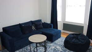 A blue sofa with a round table and a bean bag in a room with a window and radiator.