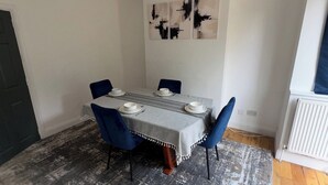 A dining area with a table set for four, blue chairs, a patterned rug, and abstract wall art.