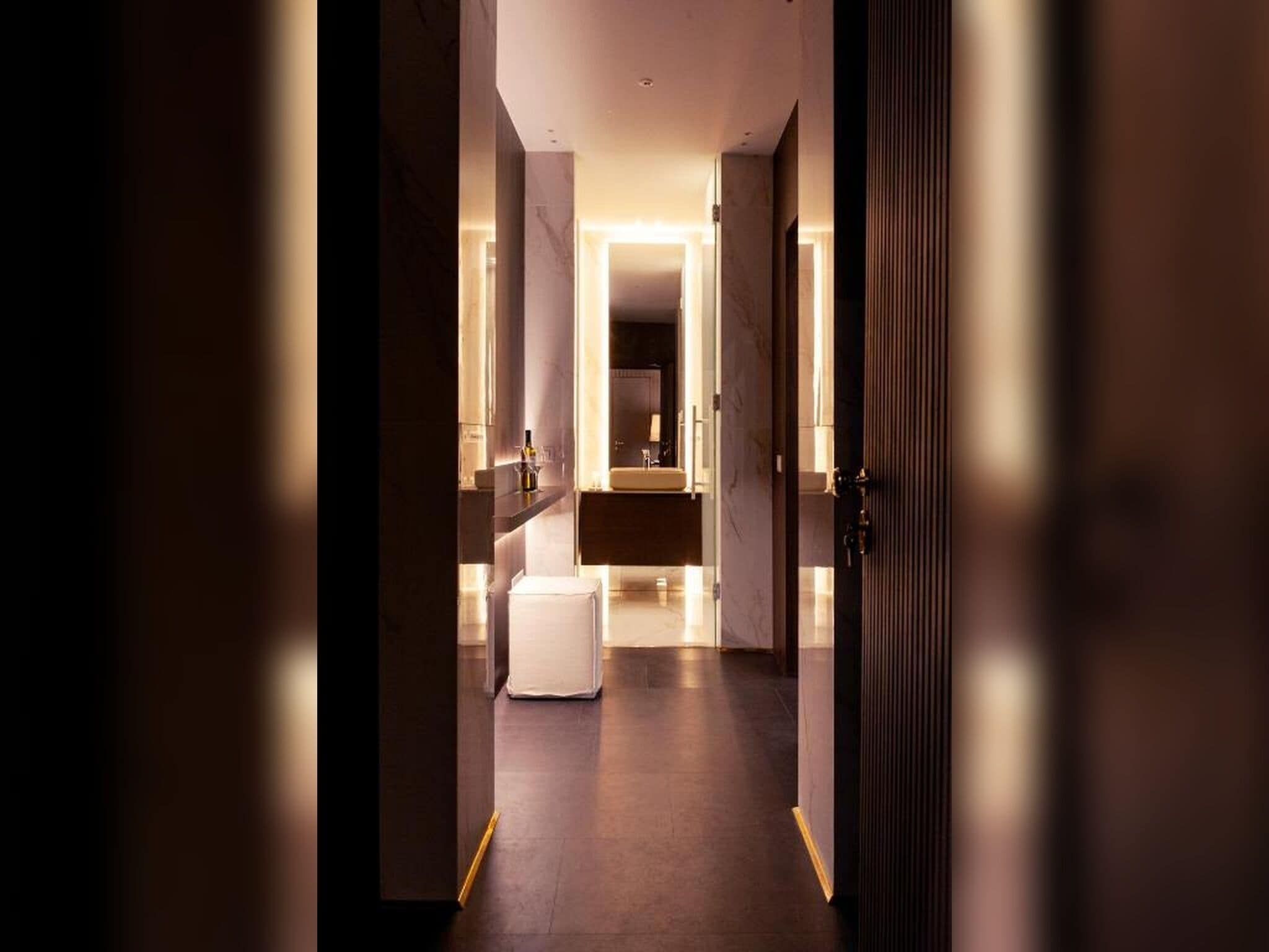 Corridoio che conduce a un bagno con il water, un lavandino e un piccolo sgabello.