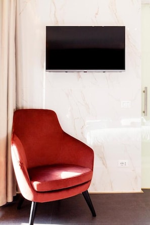 A modern interior with a red chair, a flat-screen TV mounted on a marble wall, and a glass partition. - PRESTIGE ROOM Luxury Milano  (Milan)