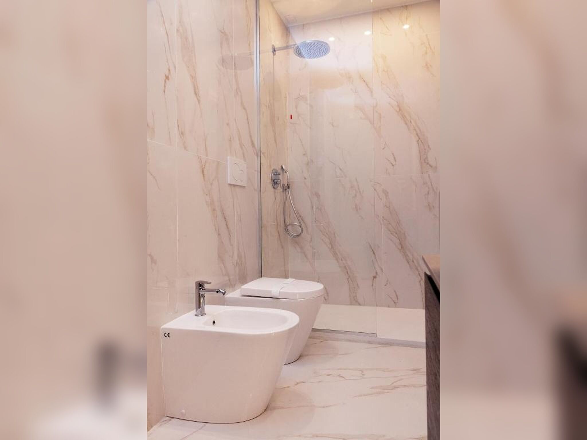 Un baño moderno con paredes de mármol, ducha y dos bidés.