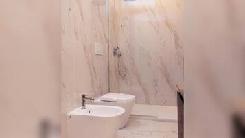 Un baño moderno con paredes de mármol, ducha y dos bidés.