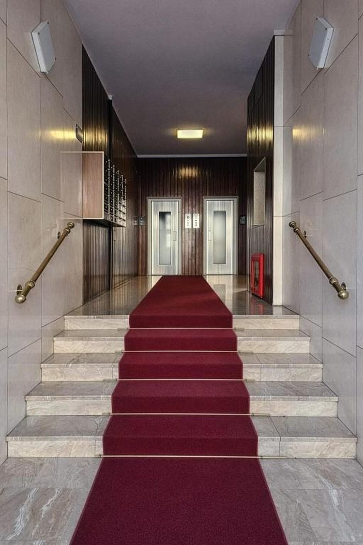 En trappe i marmor med et rødt løbende tæppe, der fører til en elevator.