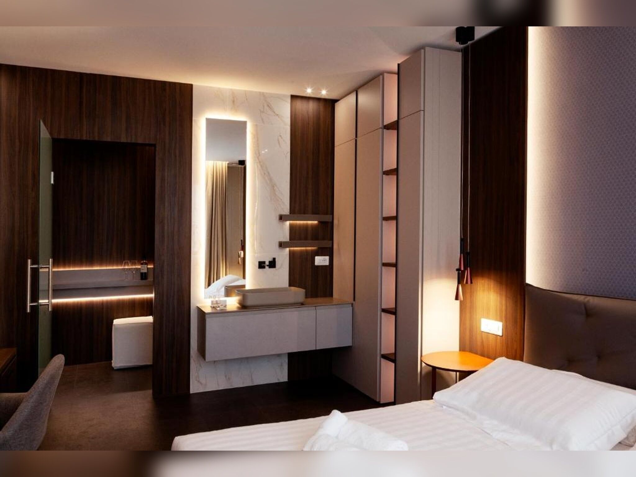 Ein modernes Hotelzimmer mit einem großen Bett, einem Schminktisch mit Spiegel, einer Sitzecke und einem Kleiderschrank.