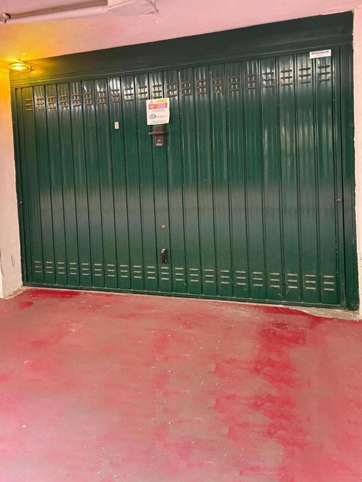 A green metal gate with a sign, a red floor, and a white wall.