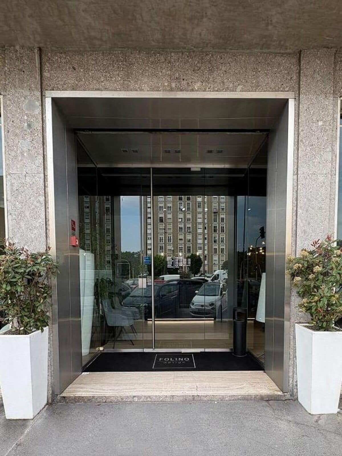 Entrada moderna de un edificio con puerta de vidrio, un felpudo negro y un letrero que dice 'FOLINO'.