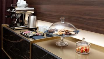 A breakfast bar with a coffee machine, a glass display case with pastries, and a jar of candies.