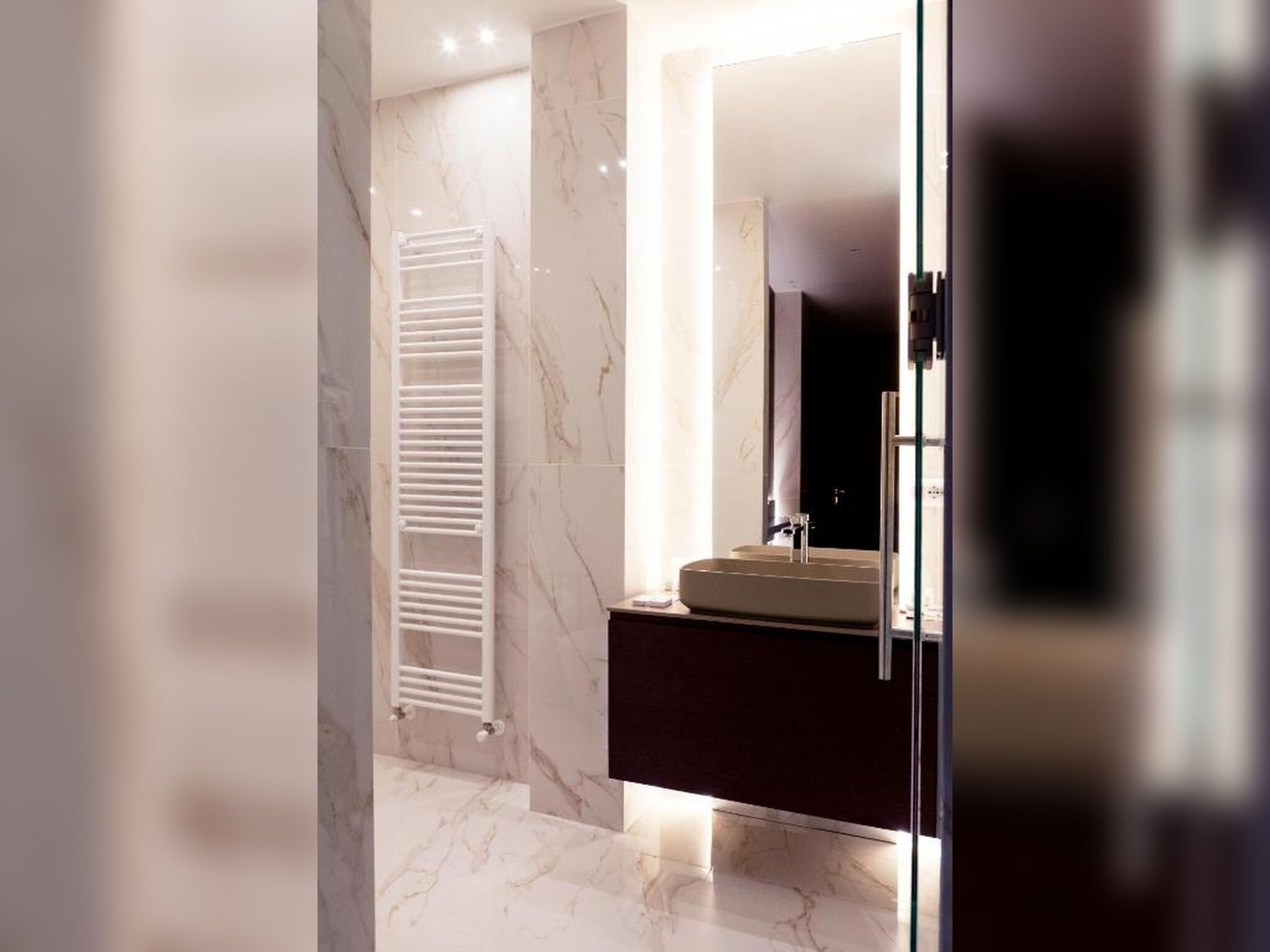 A modern bathroom with a marble floor, a white towel rack, a dark vanity, and a mirror.