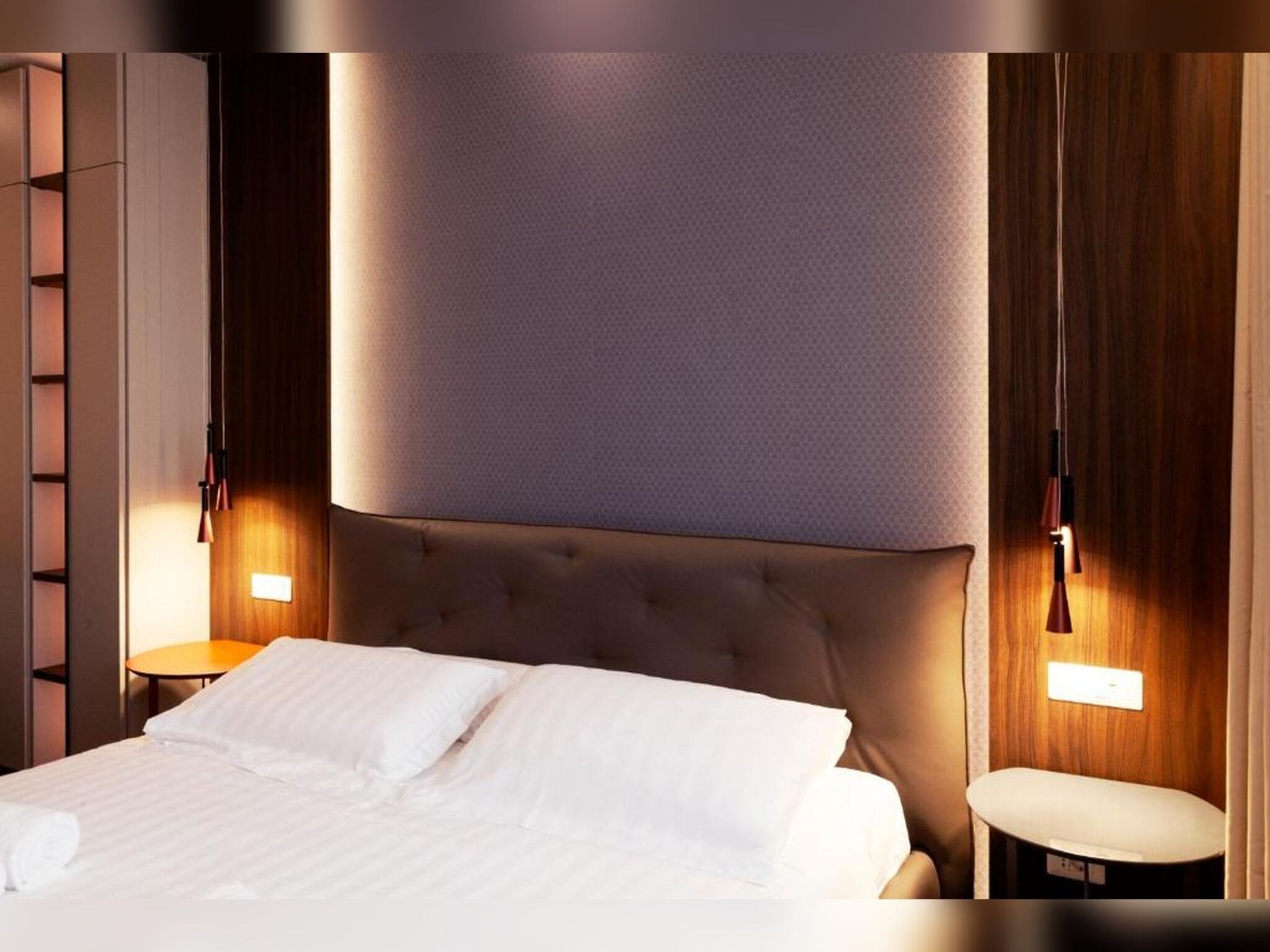 Ein Hotelzimmer mit einem großen Bett, einem Kopfteil, zwei Nachttischen und einem kleinen Hocker.