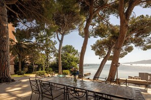 An outdoor dining area with tables and chairs, surrounded by trees and overlooking a body of water. - Villa Sud, luxury villa with sea views on Cap d’Antibes. (Antibes)
