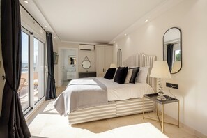 A modern bedroom with a large bed, a bedside table with a lamp, a mirror, and a view of the balcony. - Villa Sud, luxury villa with sea views on Cap d’Antibes. (Antibes)