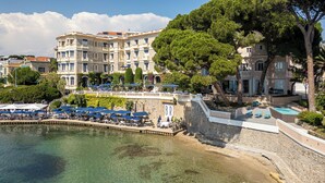 Un hotel frente al mar con piscina, zona de estar exterior y pared de piedra.