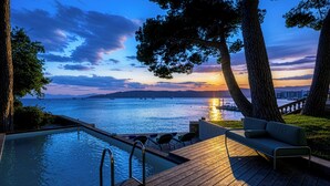 Zona de piscina con vista al atardecer sobre el agua, rodeada de árboles.