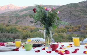 A table set for breakfast with a vase of flowers, plates of food, and glasses of orange juice. - Dar Adouss – An Authentic Retreat Amid Nature and Relaxation (Imlil)