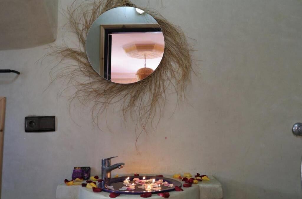 Un bany amb mirall, un lavabo i una petita taula amb espelmes i flors.
