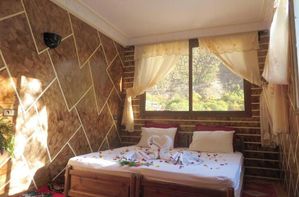 A bedroom with a bed, a window with curtains, a wall with a geometric pattern, and a wooden headboard.
