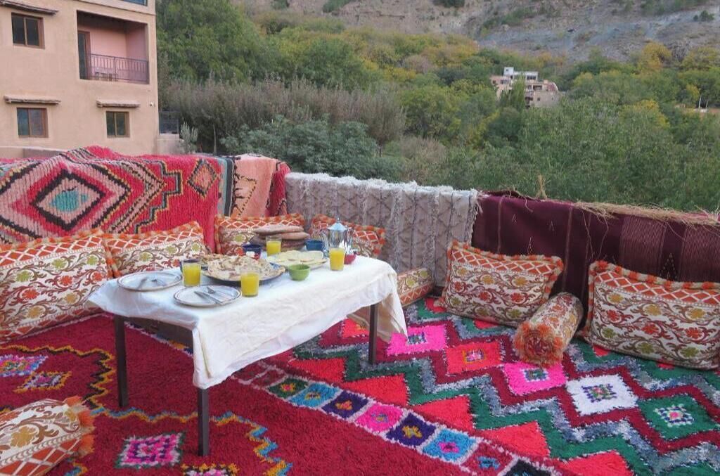 A dining area with a table set for two, surrounded by colorful patterned cushions and a vibrant rug.