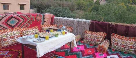 A dining area with a table set for two, surrounded by colorful patterned cushions and a vibrant rug.