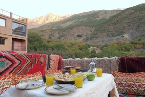 Un tavolo imbandito con piatti, posate e bicchieri di succo d'arancia, con vista su un paesaggio montuoso.