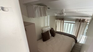 Ein gemütliches Schlafzimmer mit Bett, Kissen, einem kleinen Schreibtisch und einem Deckenventilator.