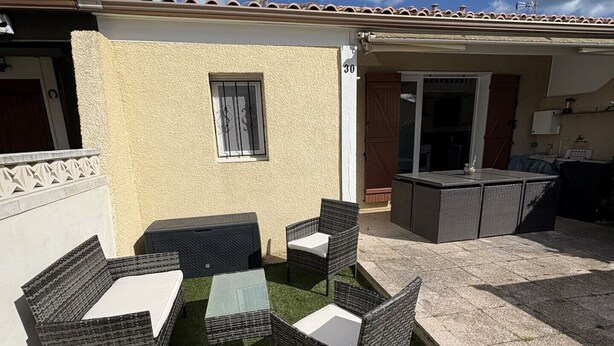 Eine Terrasss mit Korbmöbeln, einem kleinen Tisch und einem Fenster mit dekorativen Gitterstäben.