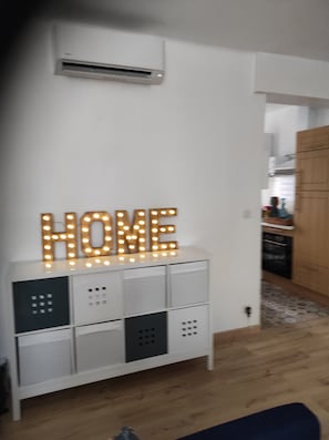 Ein weißer Lagerraum mit der leuchtenden Aufschrift 'HOME', darüber eine Klimaanlage und im Hintergrund ein Küchenbereich.