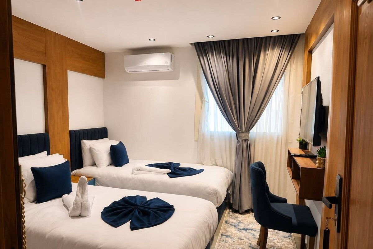 Ein Hotelzimmer mit zwei Betten, einem Schreibtisch, einem Stuhl, einem Fernseher und einer Klimaanlage.