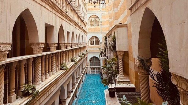 Un hotel de varios niveles con piscina central, múltiples balcones y un patio.