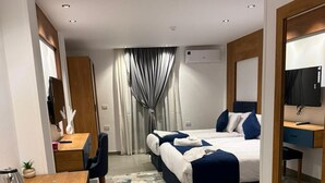 Una habitación de hotel con cama, escritorio, silla, espejo y aire acondicionado.